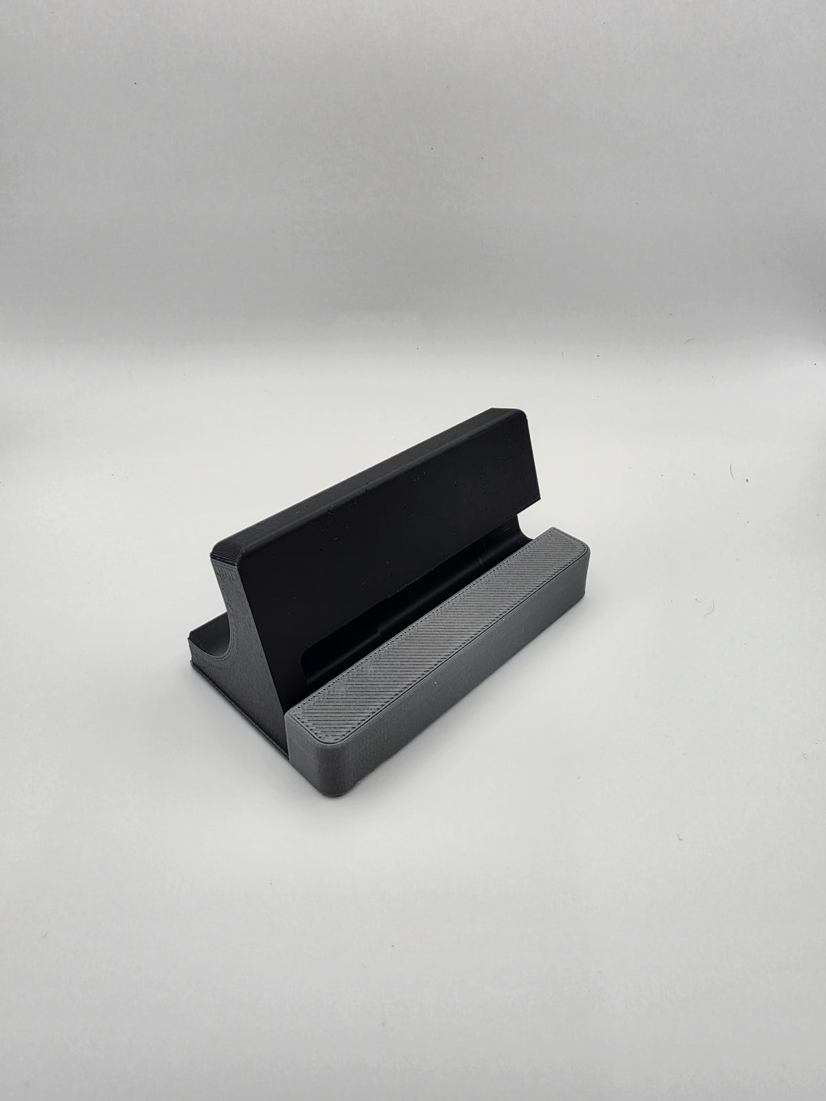 A black and gray 3D-printed charging stand, photographed on a neutral light gray background.